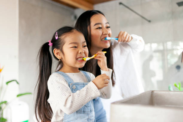 Parent and child brushing teeth using colorful toothbrushes in a bright, modern bathroom setting.