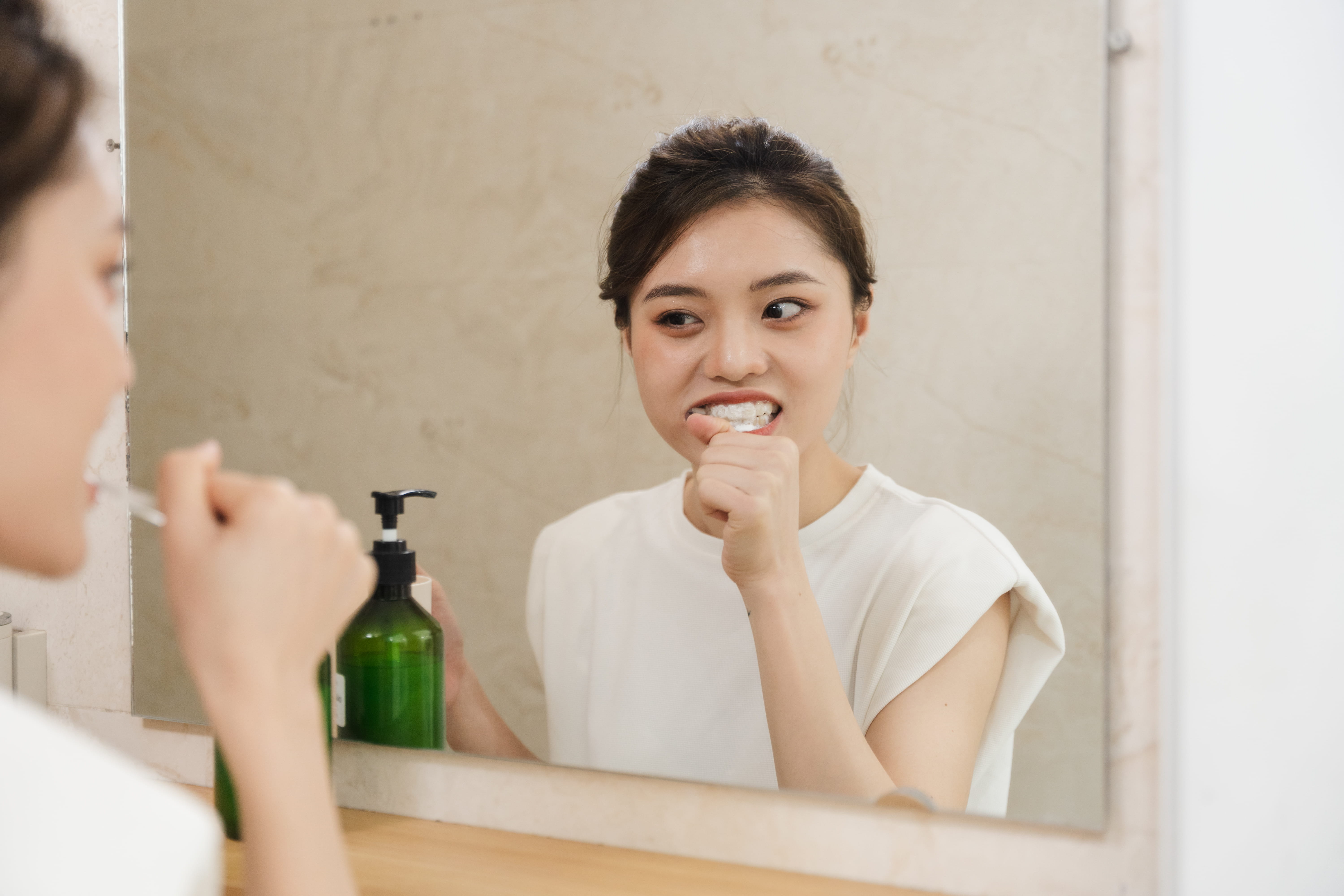 Person brushing teeth in front of bathroom mirror